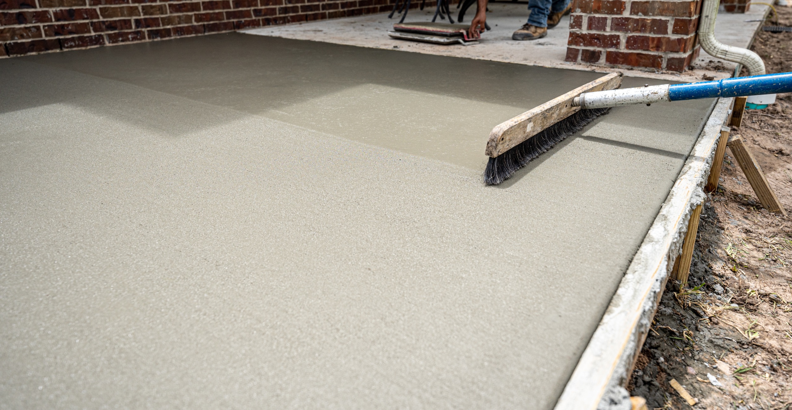 Fresh concrete slab being leveled and finished beside a home